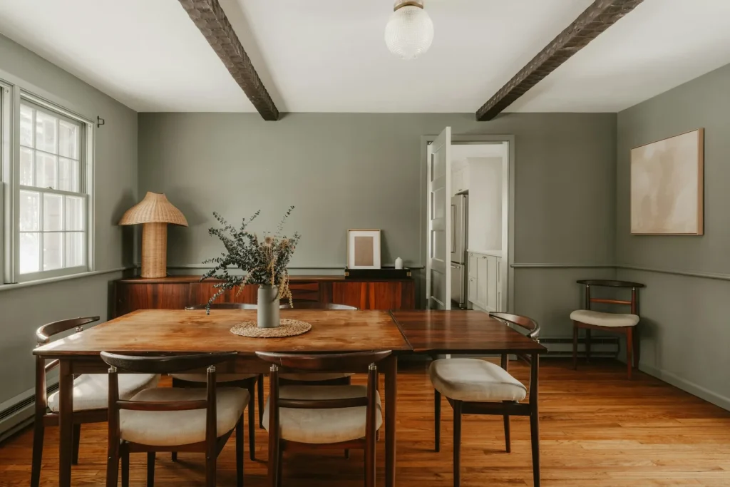 A dining room with a sage-green painted accent wall behind a timber table