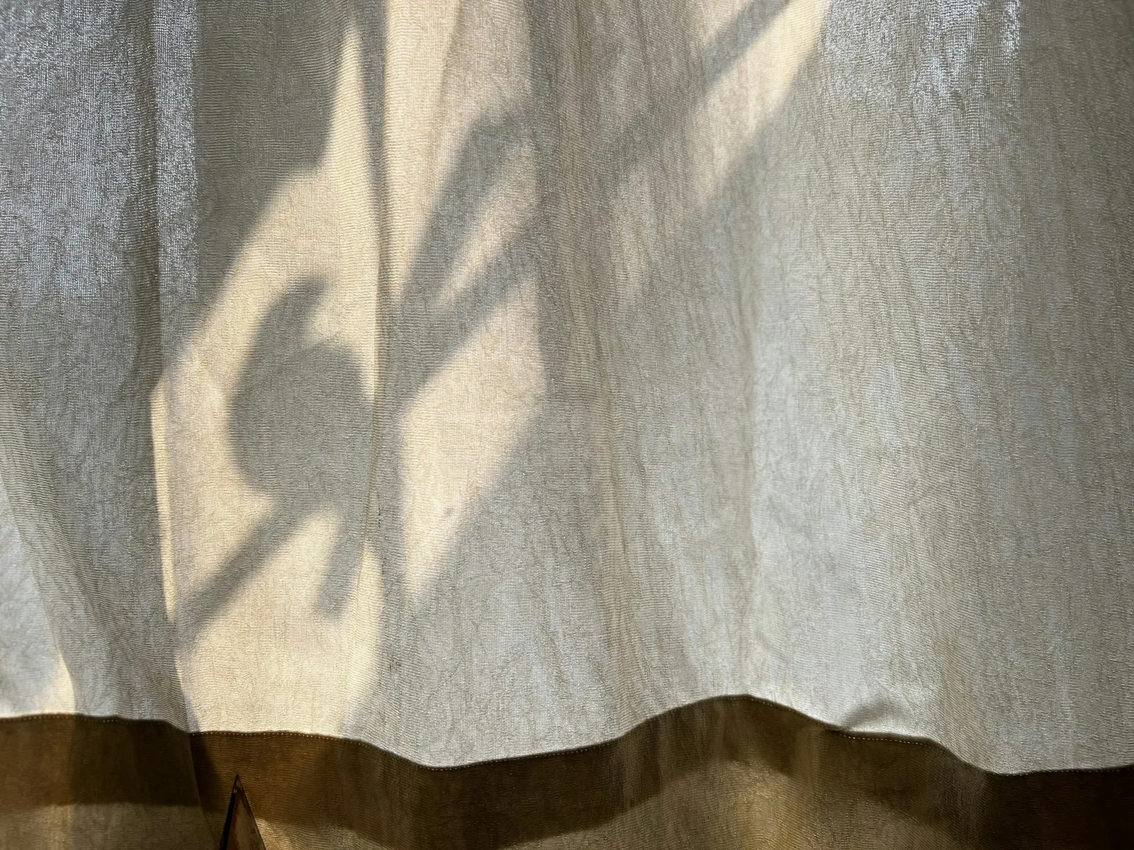 Sunlight falling across a heavy linen curtain, showing the weight of the fabric.