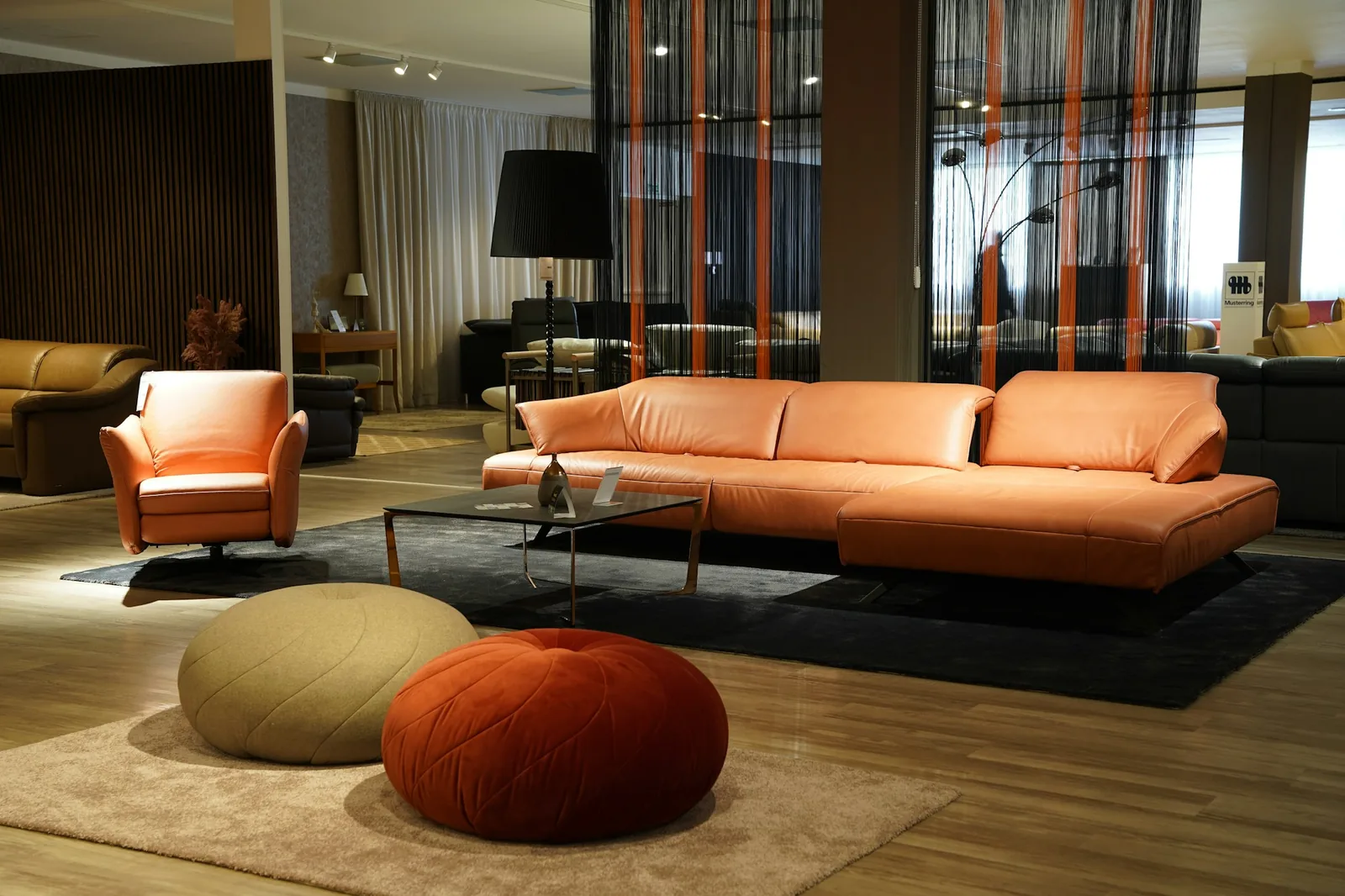 A furniture showroom with a long sofa, armchair and low ottoman arranged on a pale rug.