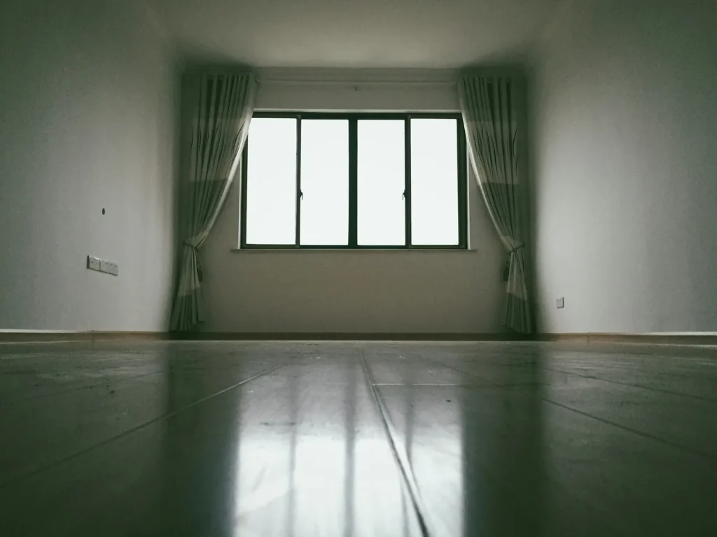 An empty room with bare walls and daylight from a tall window, before any furniture is placed.