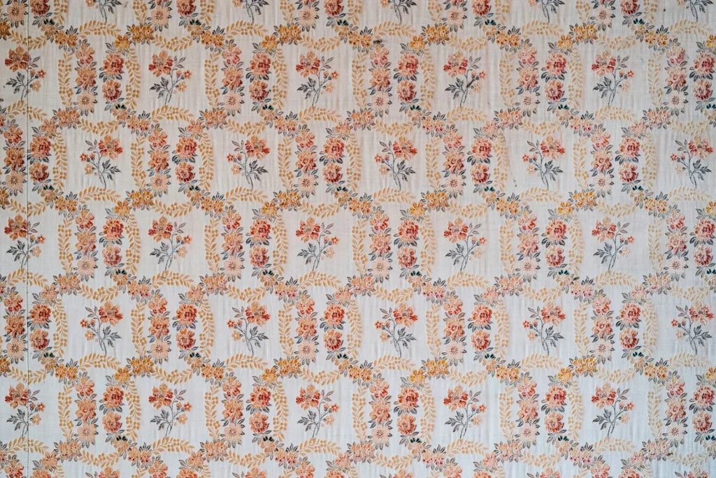 A wall hung with a repeating floral wallpaper in soft terracotta and cream.