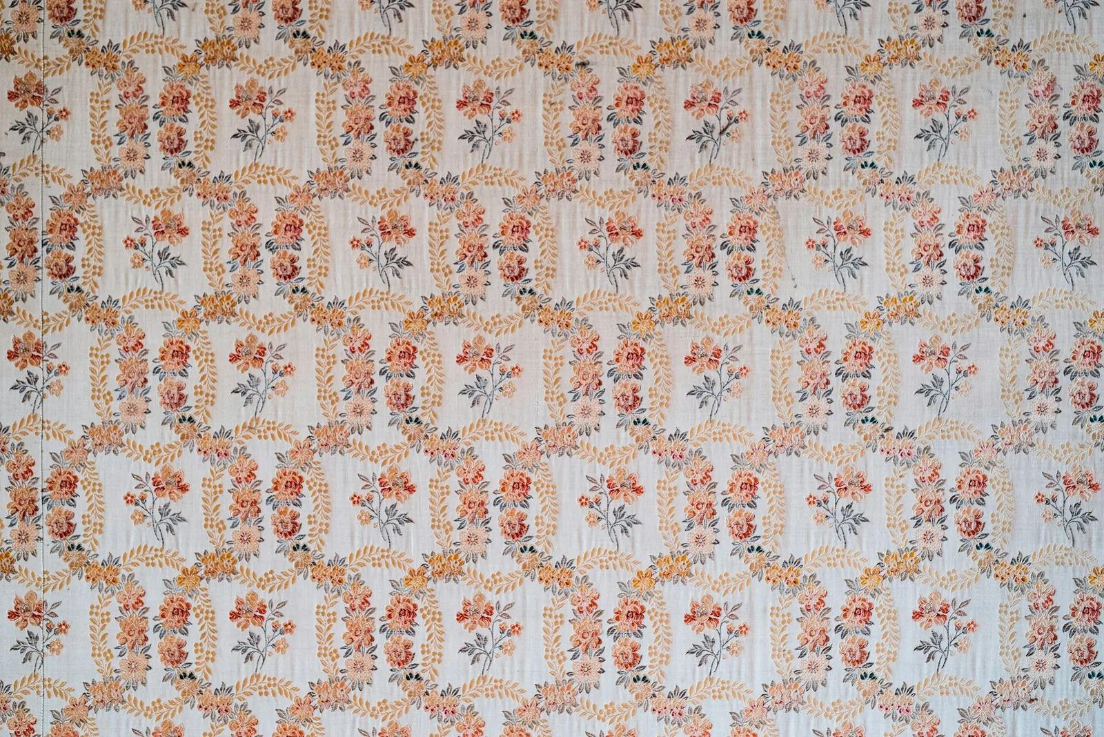 A wall hung with a repeating floral wallpaper in soft terracotta and cream.