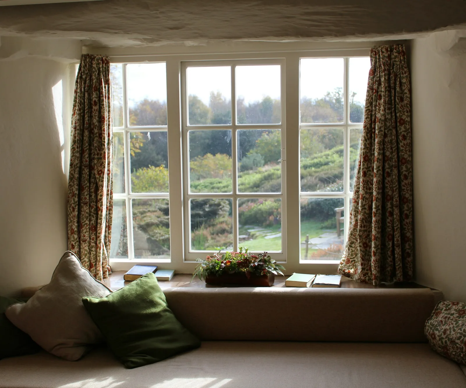 A window seat framed by full-length curtains looking onto trees.