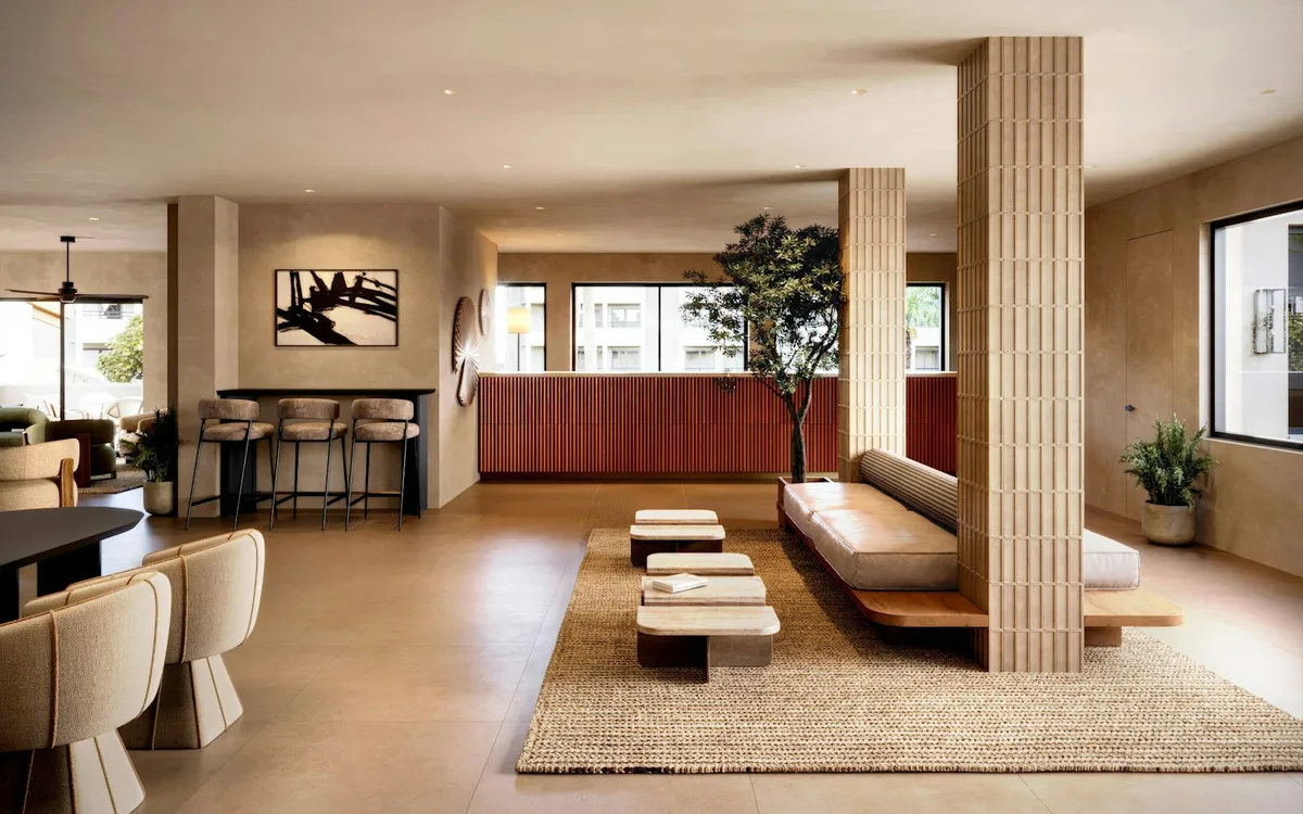 A residential amenity lounge in pale neutrals: low sofas and a long table under timber-clad ceilings, with a bar counter at the far end.