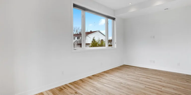 An empty bedroom before staging: bare floorboards, plain walls and an uncovered window.