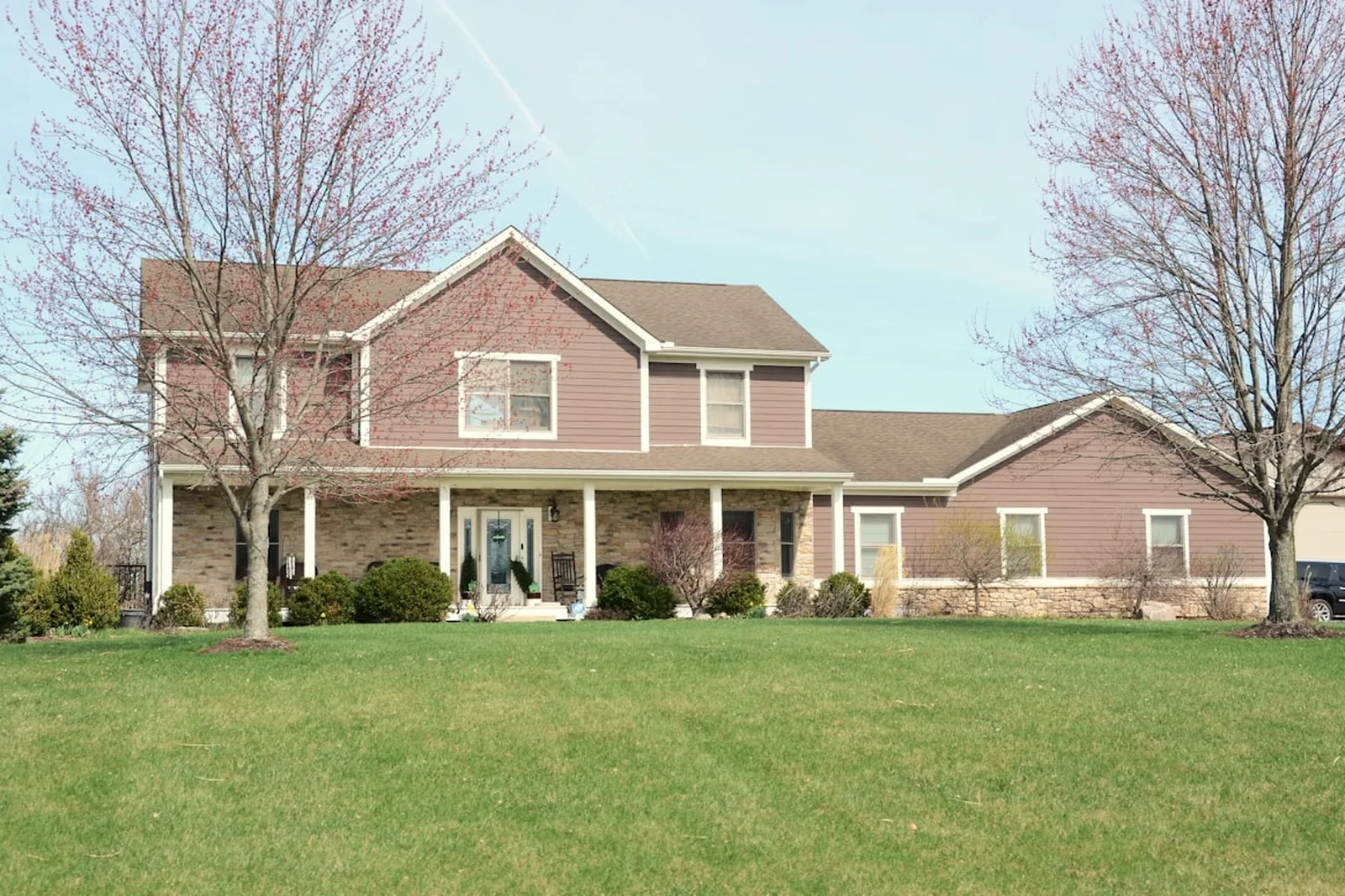 A two-storey suburban family home with a covered porch, set back behind a wide front lawn.