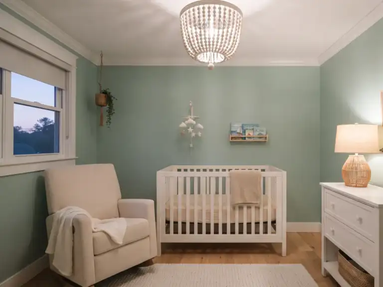 Small coastal nursery with soft sea glass green walls, a whitewashed wood bead chandelier, a white crib and a woven table lamp on a white dresser