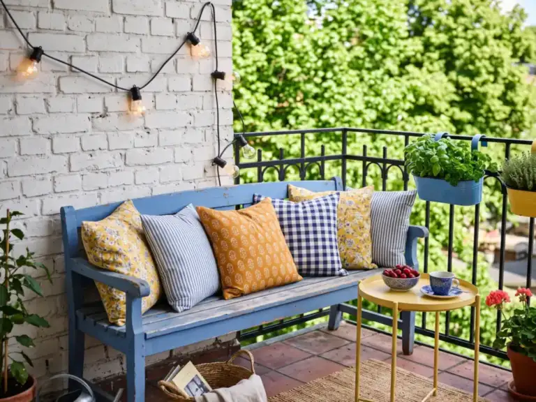 Eclectic balcony with a vintage bench painted blue, pillows in mixed yellow and blue prints, a small yellow side table and mismatched enamel planters