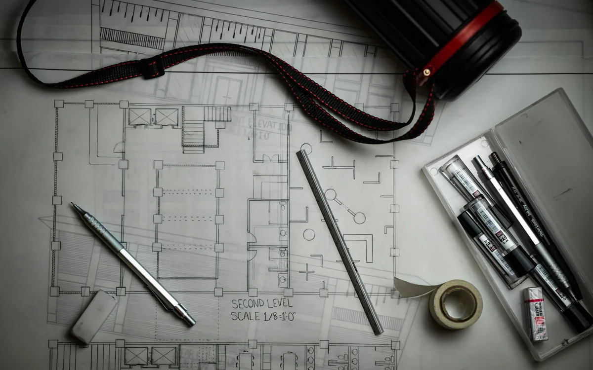 Architectural floor plans laid out on a desk with drafting pens and a scale rule.