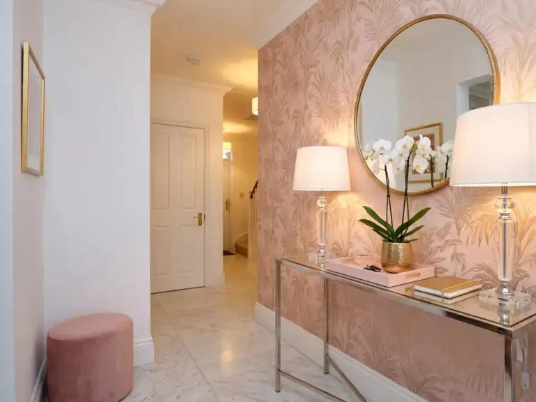 Small glam entryway with blush and gold botanical wallpaper on one wall, a mirrored console, two crystal table lamps and a white orchid in a gold pot