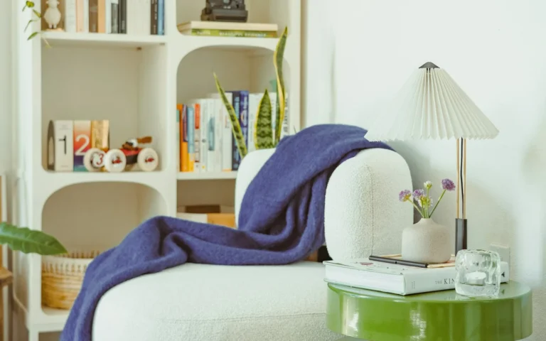 A styled living room corner: built-in shelving, books, a lamp and a folded throw.
