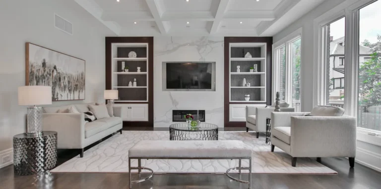 Living room staged for a listing: pale sofas and armchairs arranged around the fireplace, lit by a bank of windows.