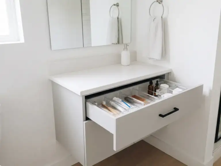 Small minimalist bathroom with a light gray vanity, its top drawer open to show clear organizers, and a bare white counter holding one soap dispenser