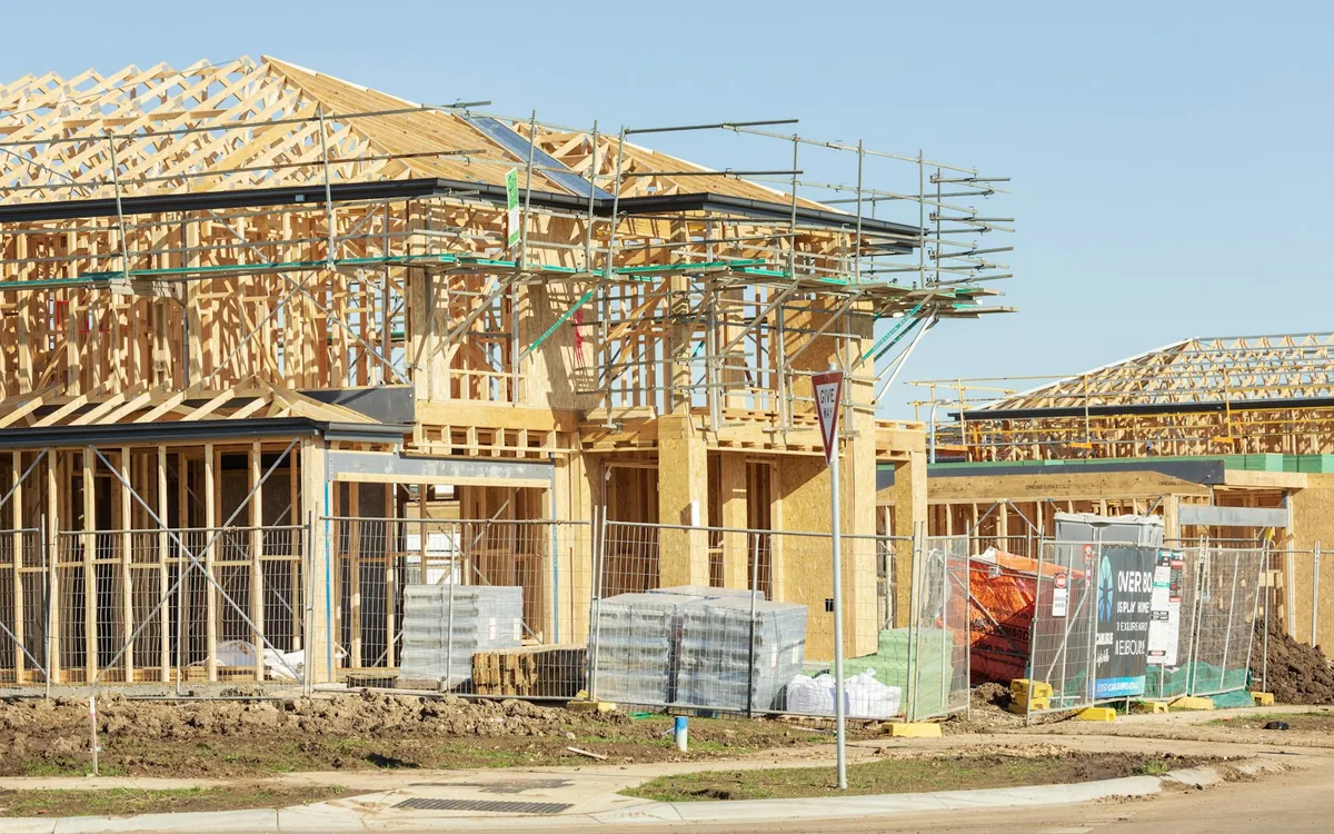 A row of new houses still in timber frame on a development site, scaffolding up and materials stacked at the kerb.