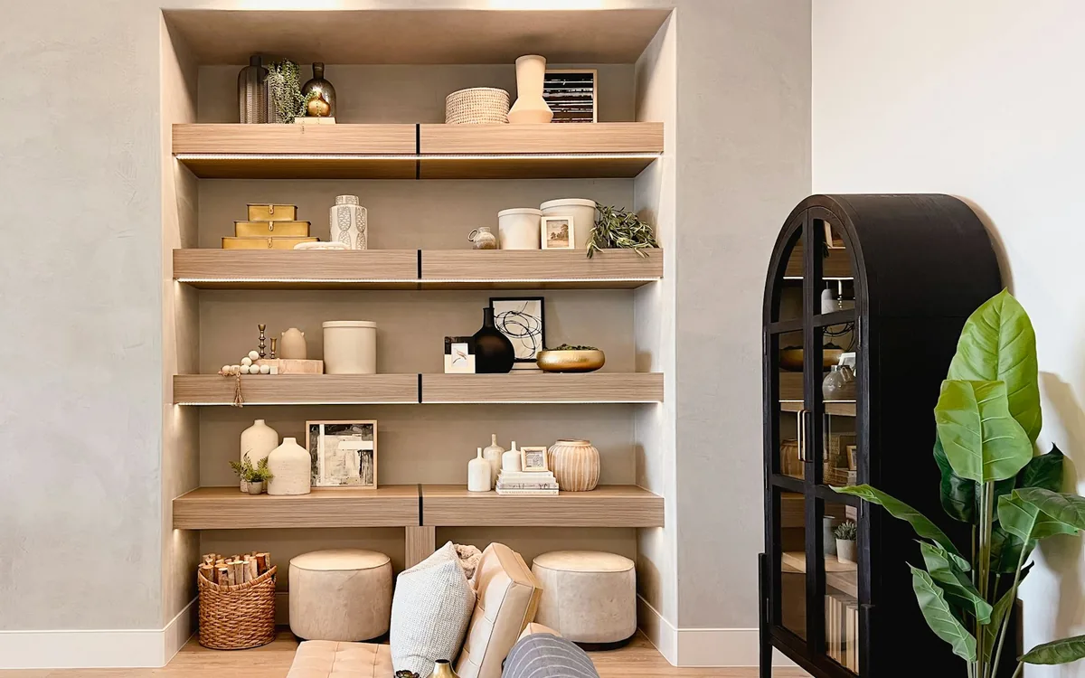 A sales gallery display wall: pale timber shelving styled with ceramics, books and candles beside a black glazed cabinet.