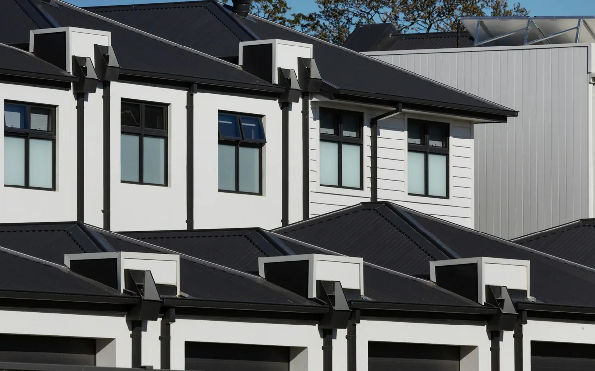 A row of newly built white townhomes with dark gabled roofs and integral garages.
