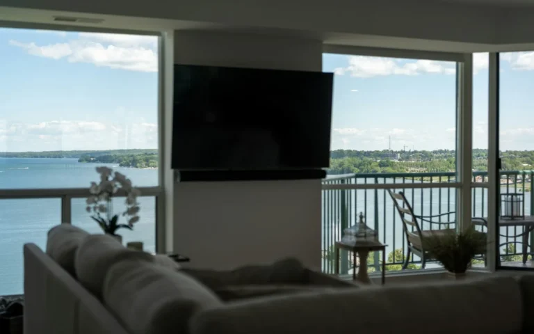 A television mounted on a living-room wall beside tall windows.