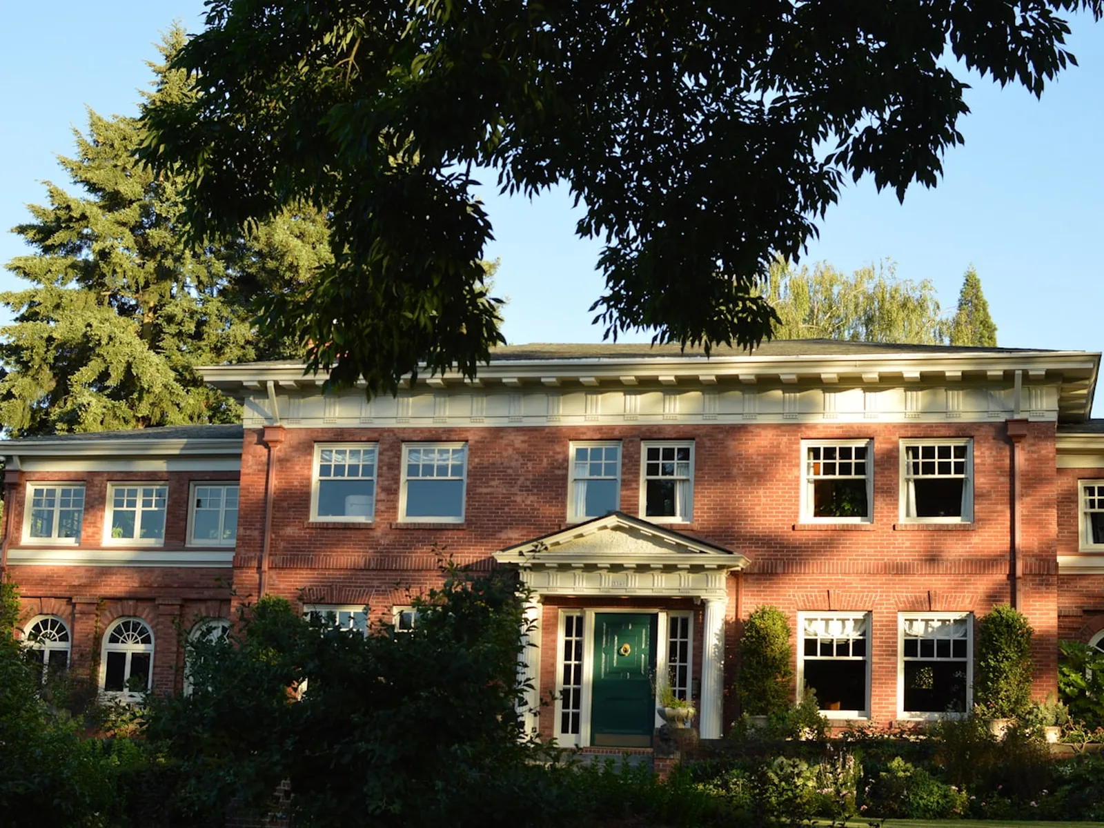 An established red-brick house with a columned entrance, framed by mature trees.
